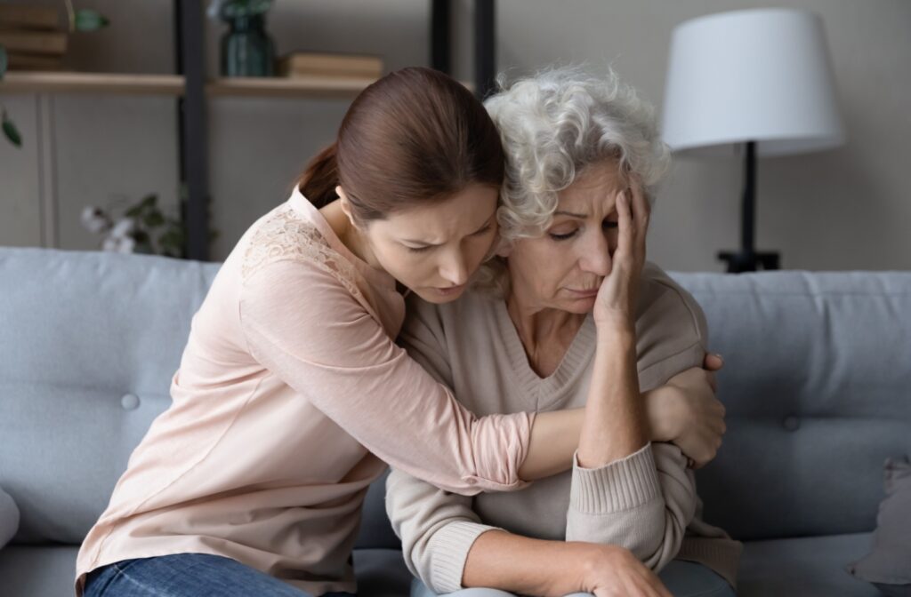 A caring adult hugs their distressed older parent in an attempt to comfort them as they struggle to support themselves