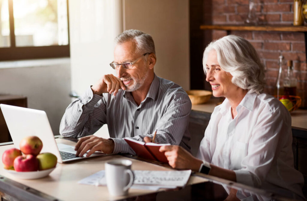An older couple sitting together at their dining room table and checking out assisted living communities online.