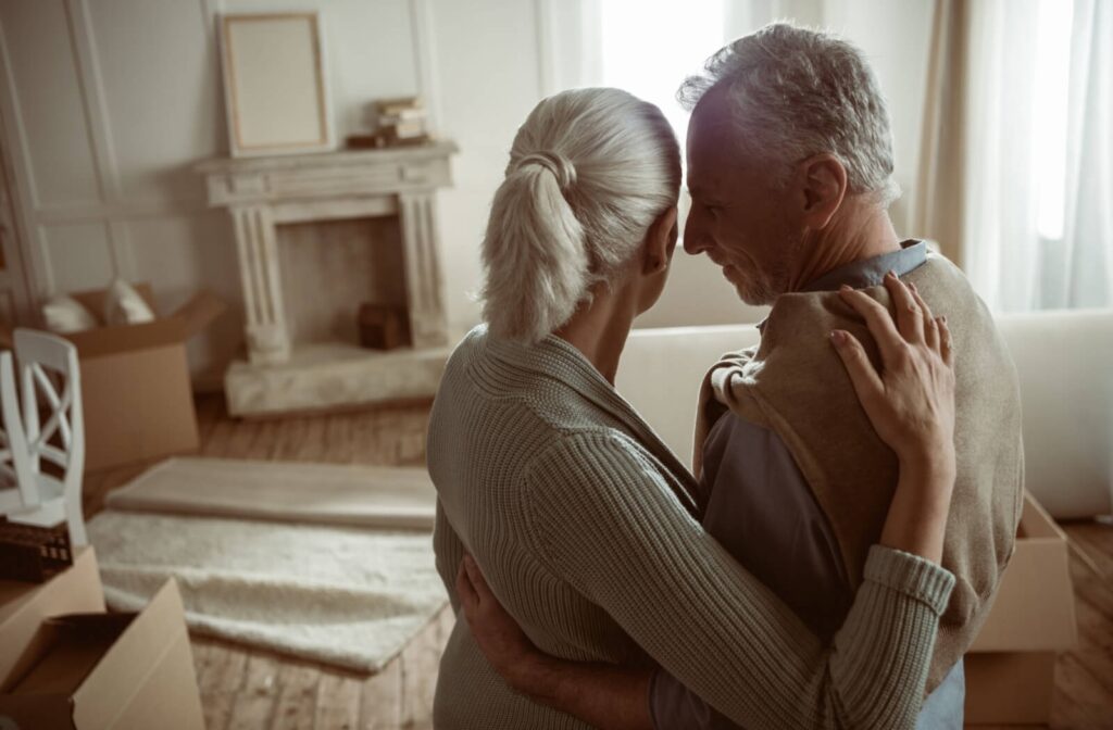 Two older adults share a tender moment and touch their faces together mid-way through packing up their living room