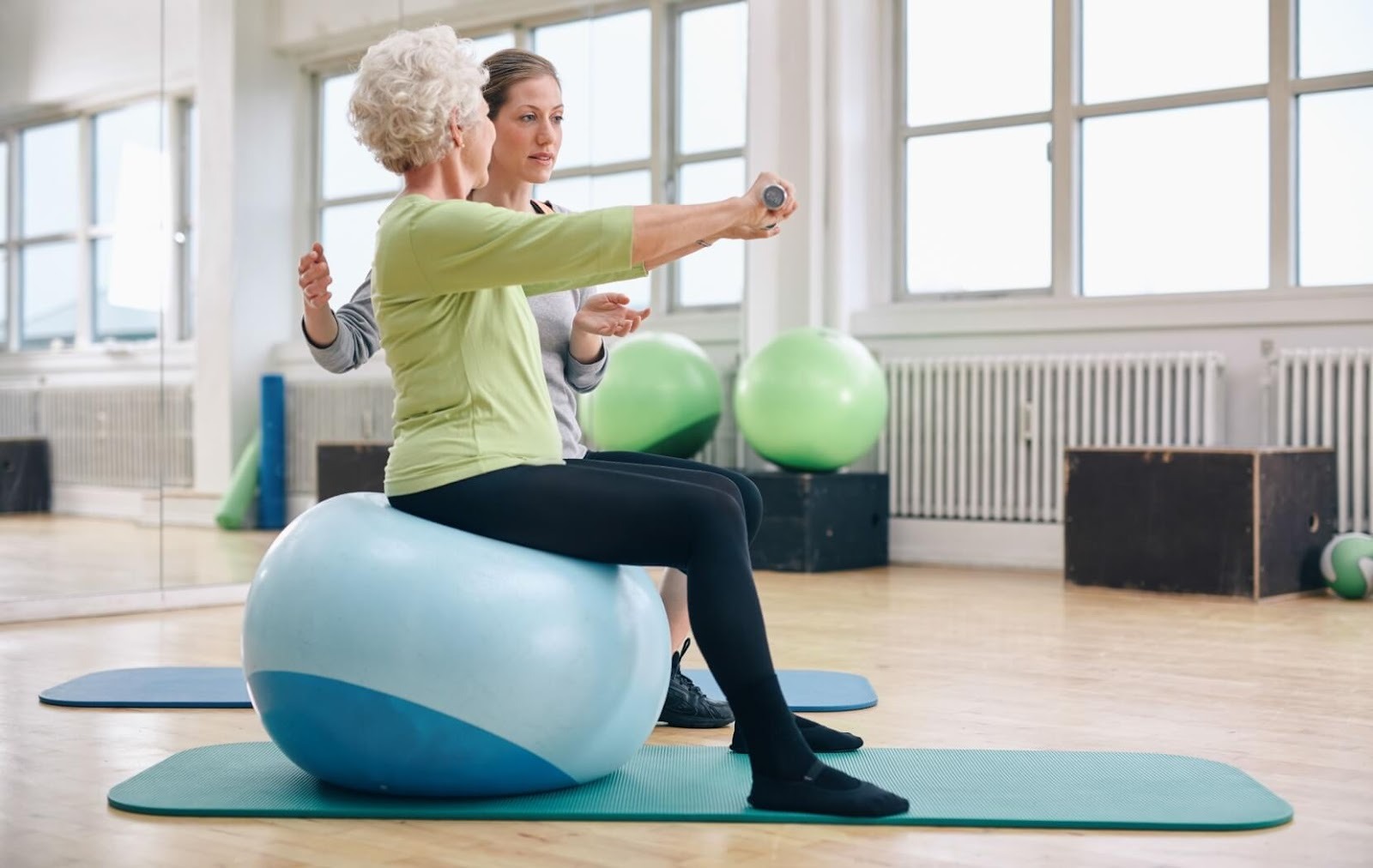 A caregiver helps a senior with an exercise while balancing on an exercise ball.