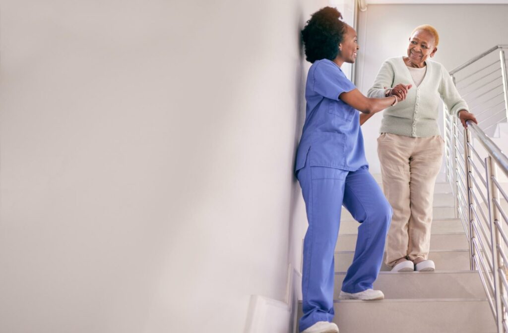 A caregiver helps a smiling assisted living resident down a flight of stairs, reducing fall risk